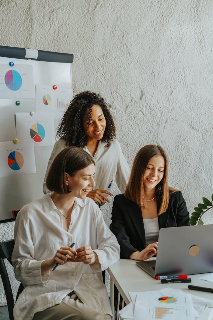 Three businesswomen collaborate with graphs and a laptop in a modern office setting.